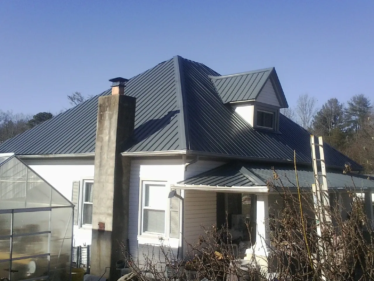 Dark blue standing seam metal roof on a white farmhouse with dormer — Slate & Tile Roof Repair by Roofing Brothers in Spearfish