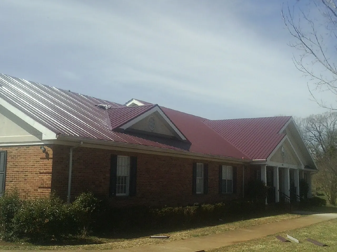 Red metal roof with gabled entries on a long brick building, from a Hail Damage Roof Repair job in Spearfish
